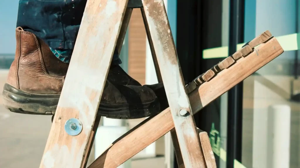 A person standing on the top rung of a half open wooden ladder