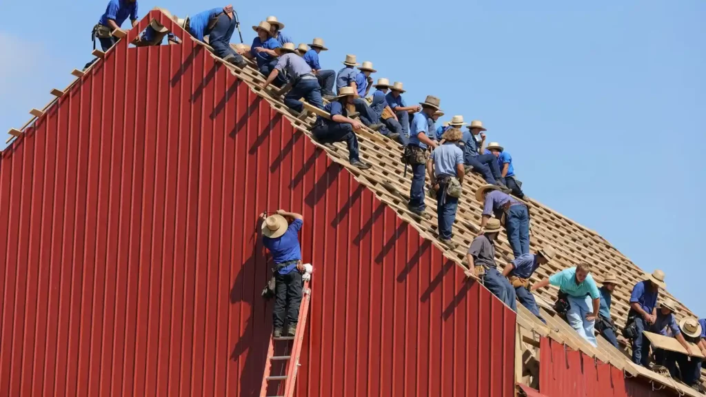 A team of craftsmen is constructing the roof of a red barn