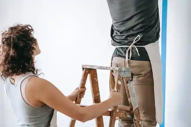 A woman holding the ladder steady while a man is on it. 