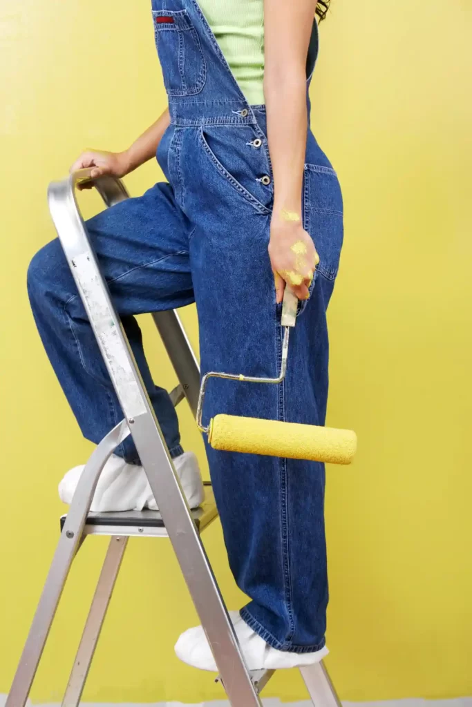 Woman standing on stepladder holding paint roller